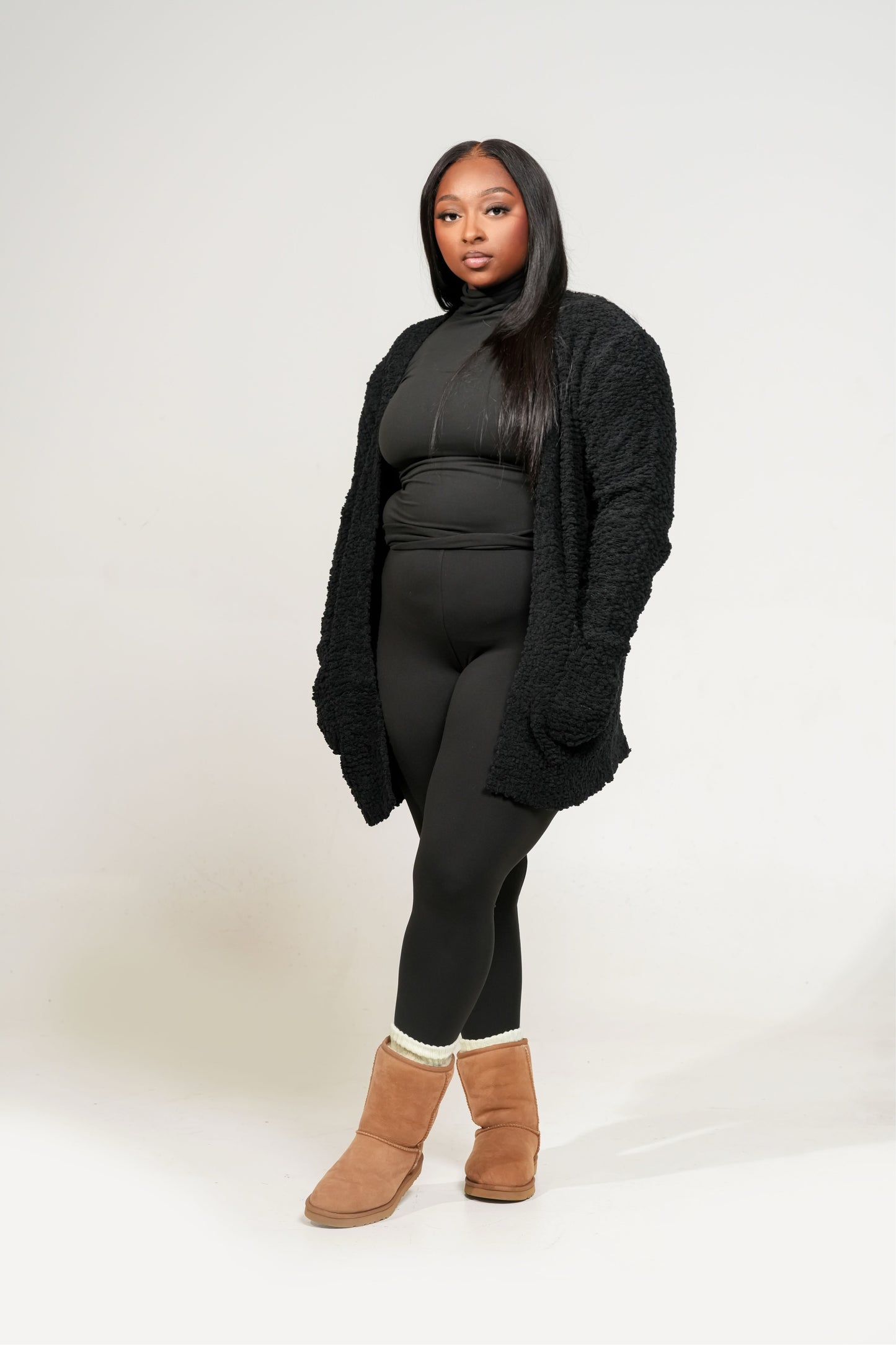 Person wearing a black outfit with a textured cardigan and brown boots on a white background