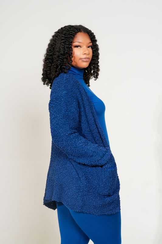 Woman wearing a blue sweater and pants against a white background. Cozy Pop Cardigan designed for soft, effortless living. Made from premium popcorn knit, this layer brings warmth, texture, and everyday comfort into one cozy essential.