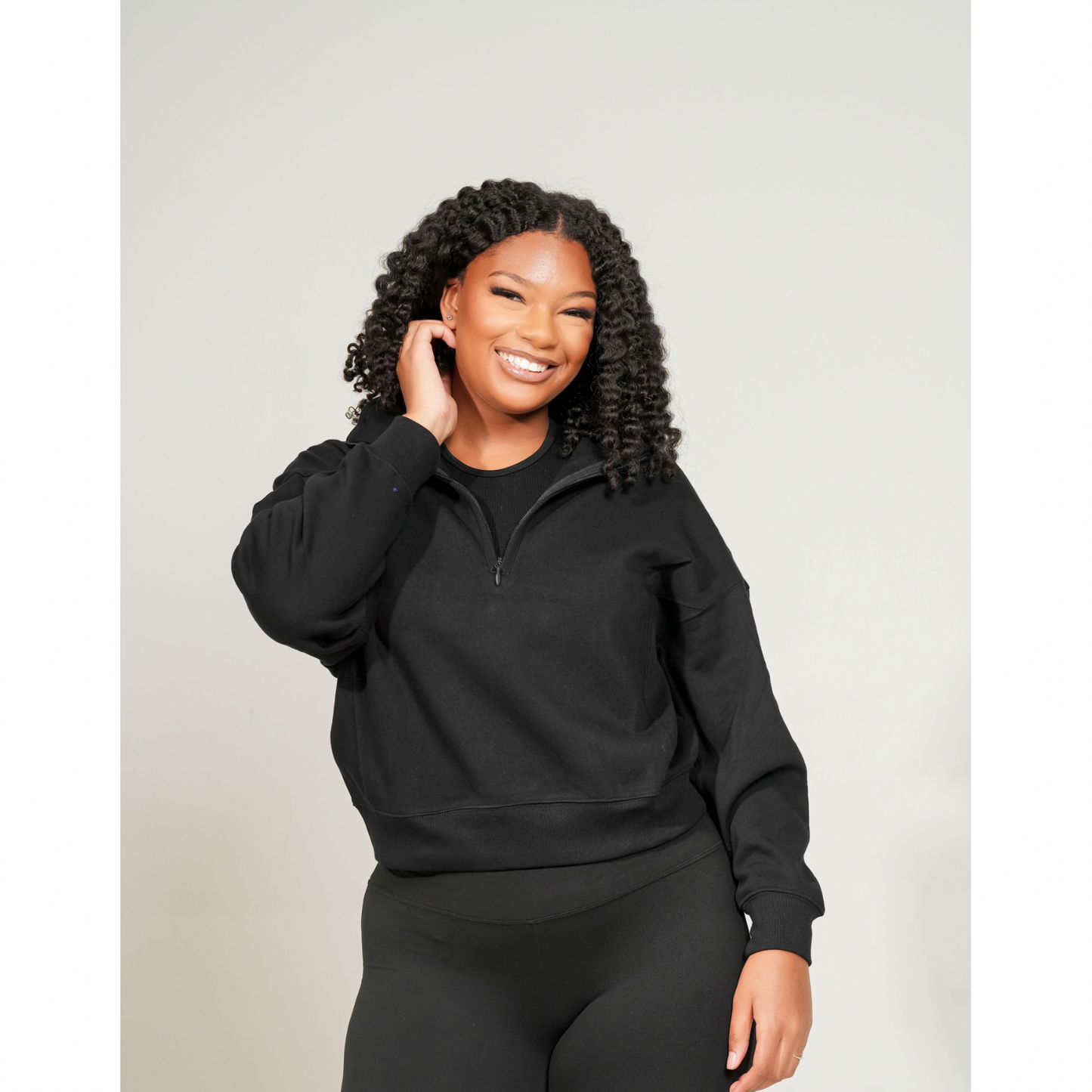 Woman wearing a black hoodie and leggings against a light gray background. FLEECE HIGH NECK HALF ZIP SWEATSHIRT