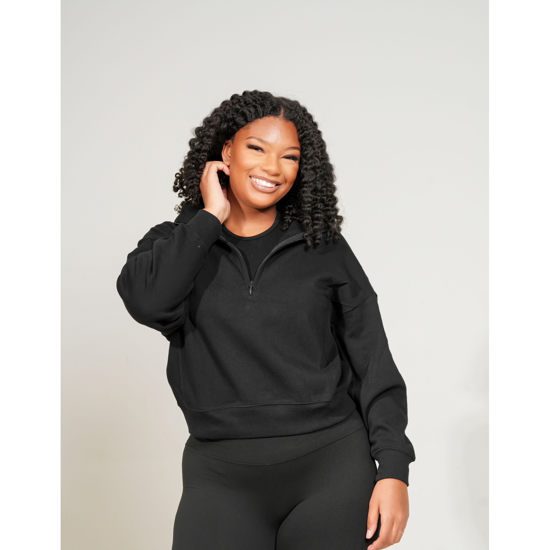Woman wearing a black hoodie and leggings against a light gray background. FLEECE HIGH NECK HALF ZIP SWEATSHIRT
