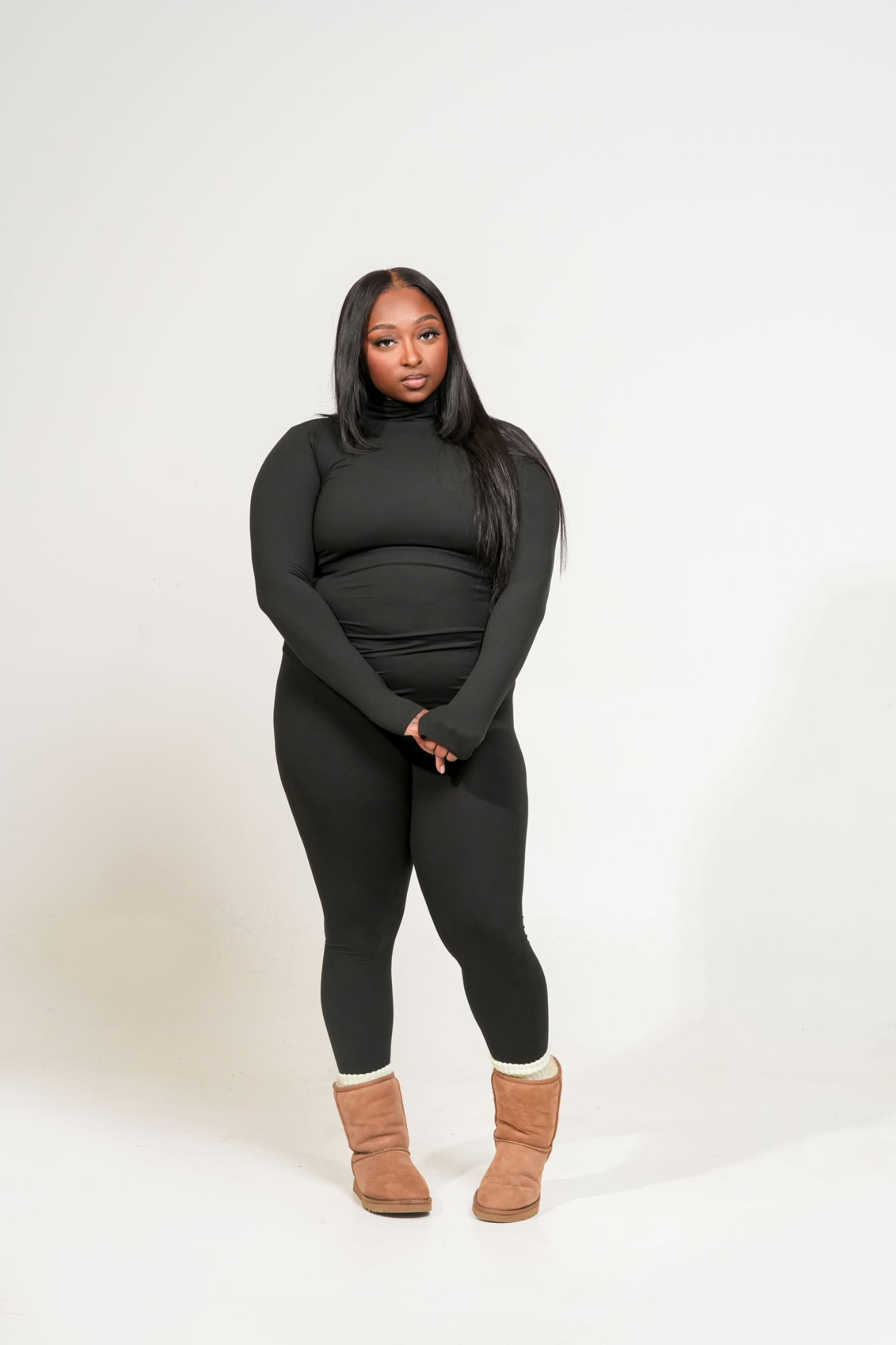 Person wearing a black MICROFIBER MOCK NECK TOP & LEGGINGS SET. outfit with brown boots on a white background