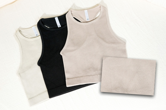 Three tank tops in beige, black, and beige with a folded beige fabric on a white background. RIBBED SEAMLESS HIGH-NECK CROPPED TANK TOP. BLACK, mocha, sand beige